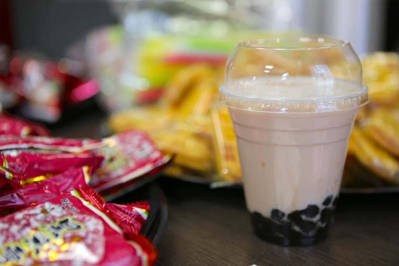a cup of bubble tea with black bubble and brown liquid in front of red wrappers