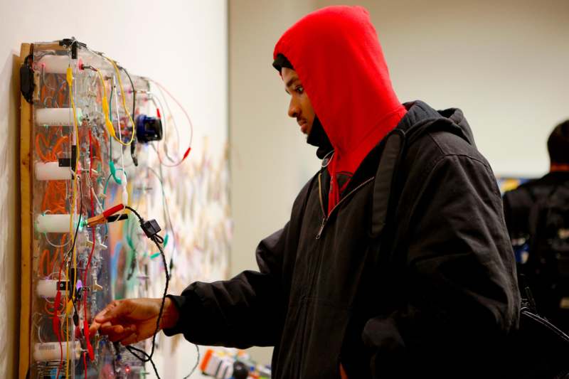 a man in a red hoodie looking at wires on a wall