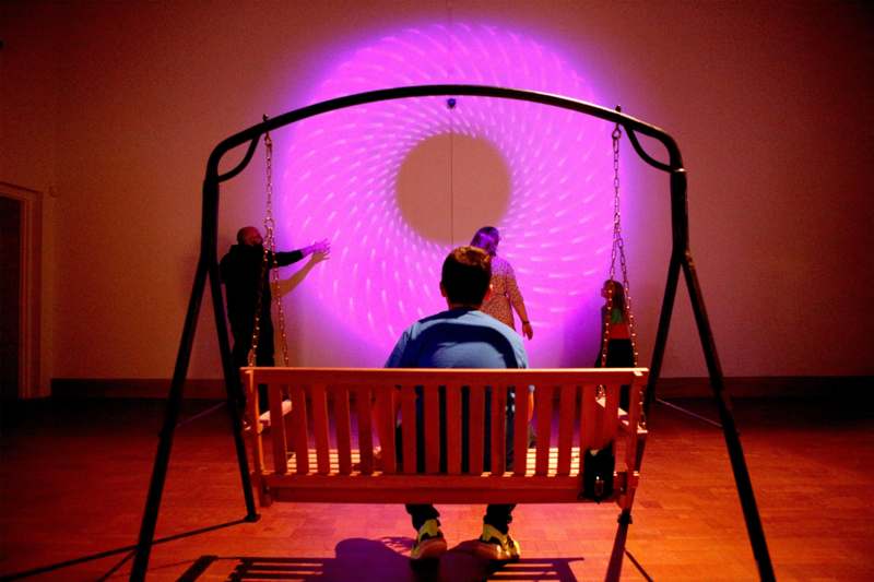 a man sitting on a swing in front of a purple light