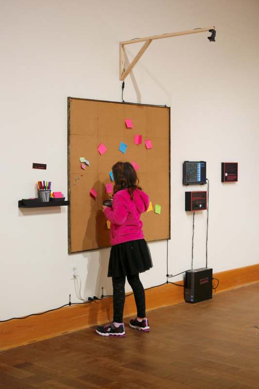 a girl in a pink jacket and black skirt standing next to a cork board with sticky notes
