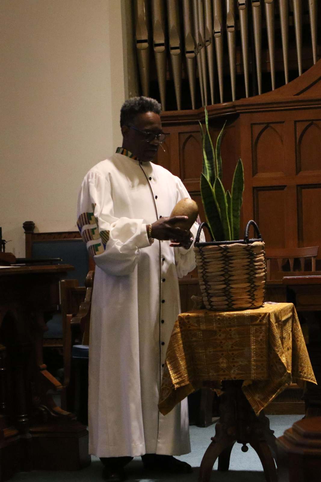 a man in a white robe standing next to a basket with a plant