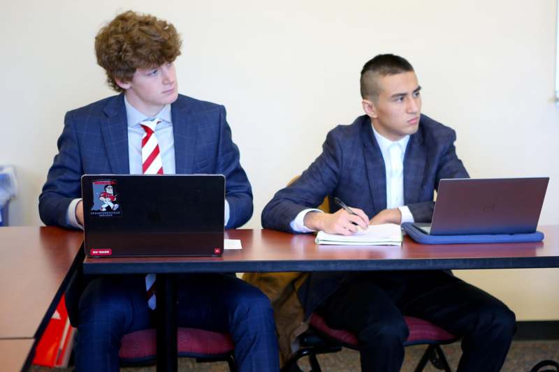 two men sitting at a table with laptops and notebooks
