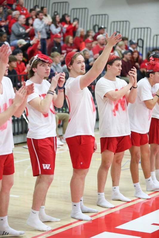 a group of men in red shirts and shorts standing on a court with their hands up