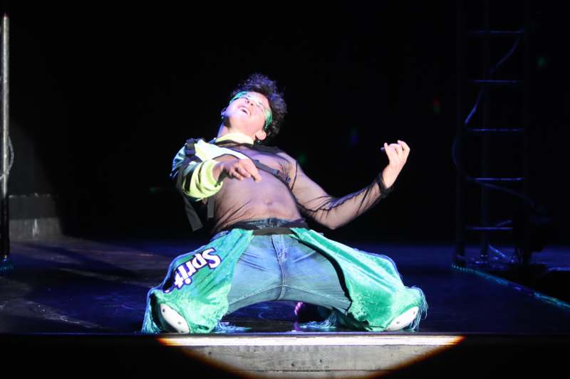 a man in a mesh shirt and green pants on a stage