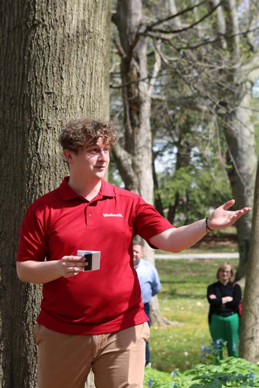 a man in a red shirt holding a cup and standing next to a tree