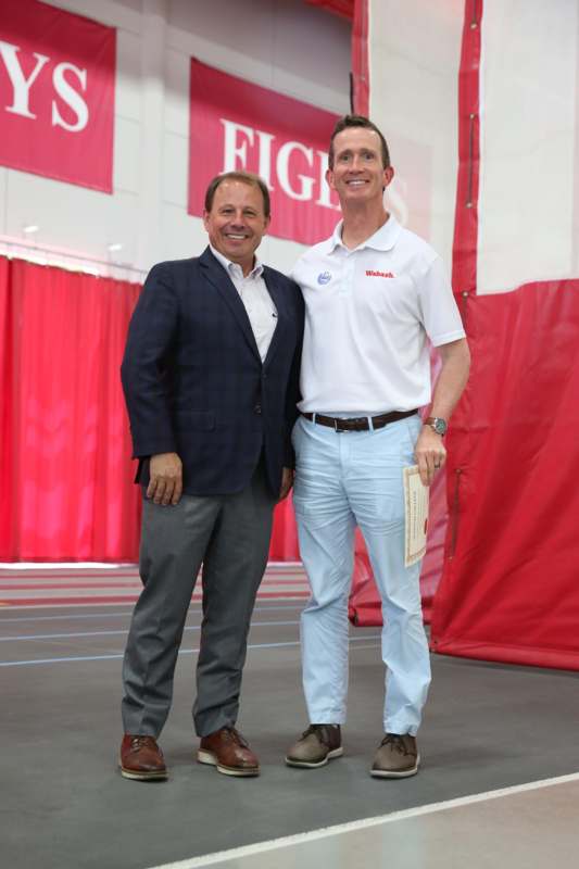 two men standing together in front of a red curtain