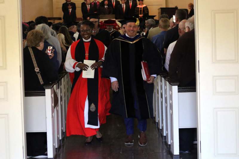 a man and woman in robes and gowns walking down a aisle