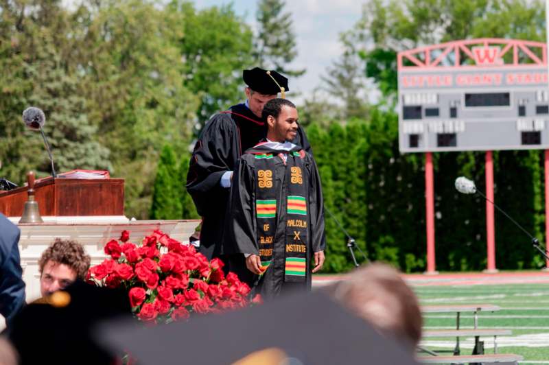 a man in a graduation gown standing next to another man