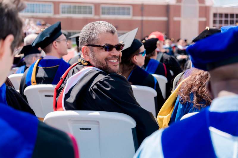 a man in a graduation gown sitting in a row