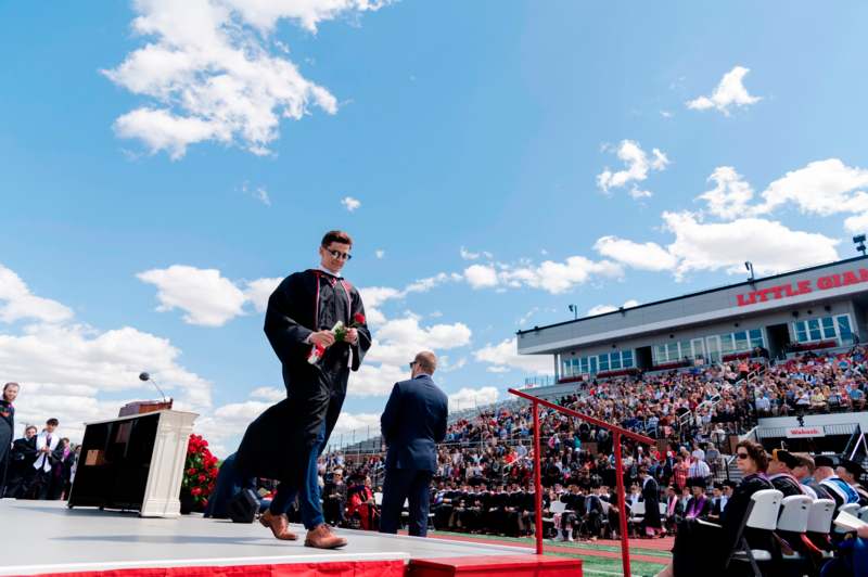 a man in a graduation gown walking on a stage with a crowd watching
