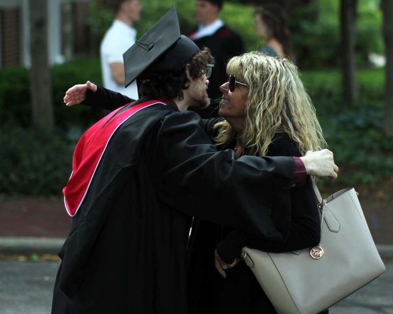 a man in a graduation gown hugging a woman