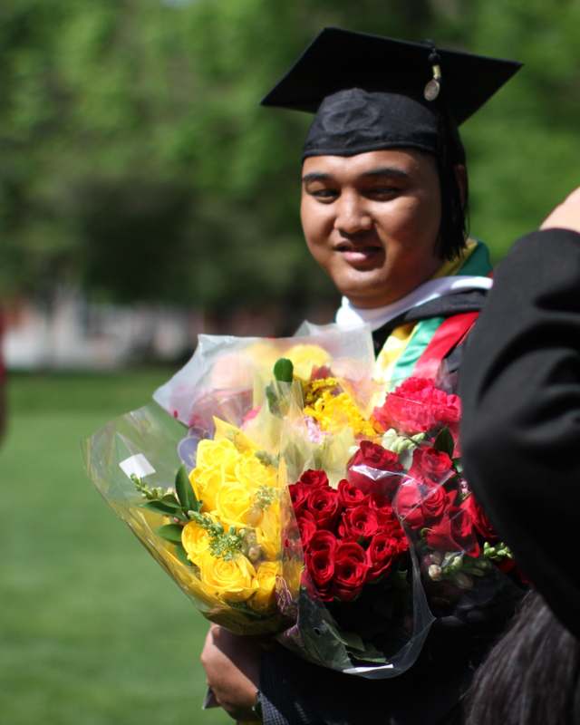a man in a graduation cap and gown holding flowers