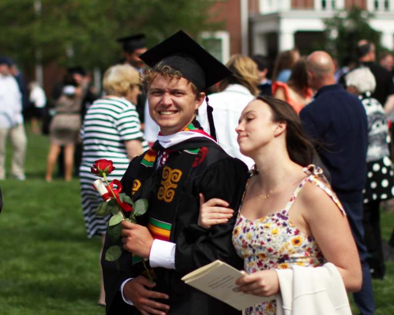 a man in a graduation gown holding a rose and a woman in a crowd