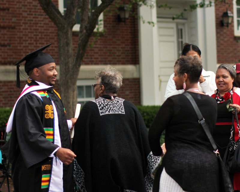 a man in a graduation gown talking to a group of people