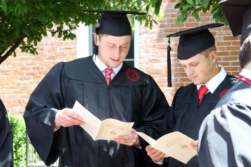 a group of men in graduation gowns and caps looking at papers