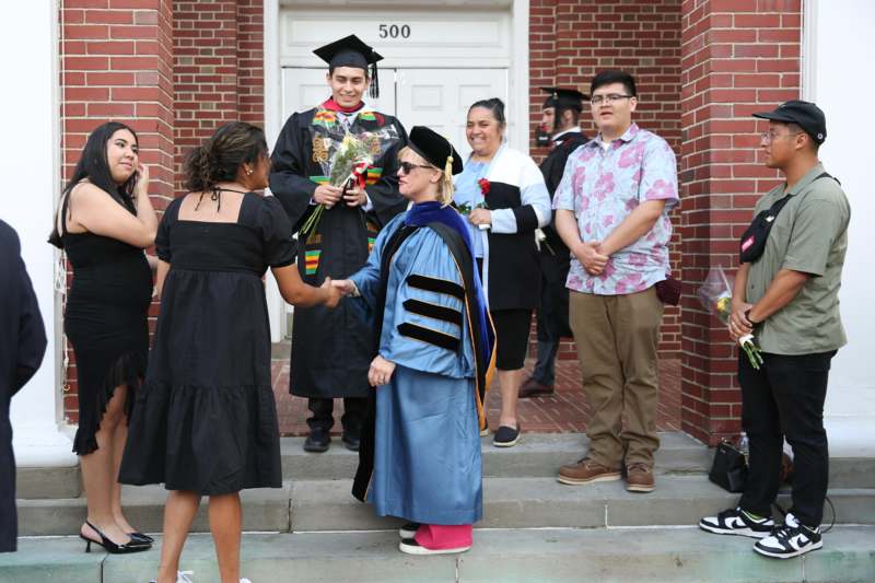 a woman shaking hands with a man in a graduation gown