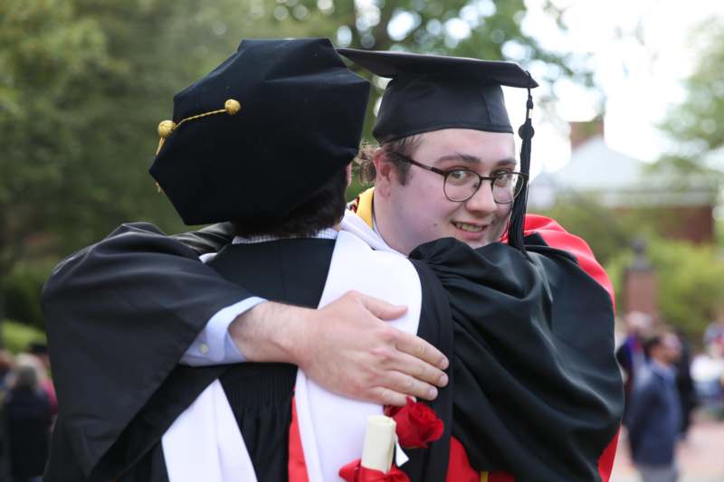 a man in a graduation gown hugging another man