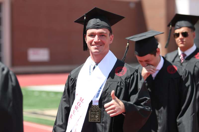 a man in graduation gown and cap giving a thumbs up