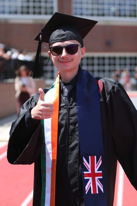 a man in a graduation gown and cap giving a thumbs up