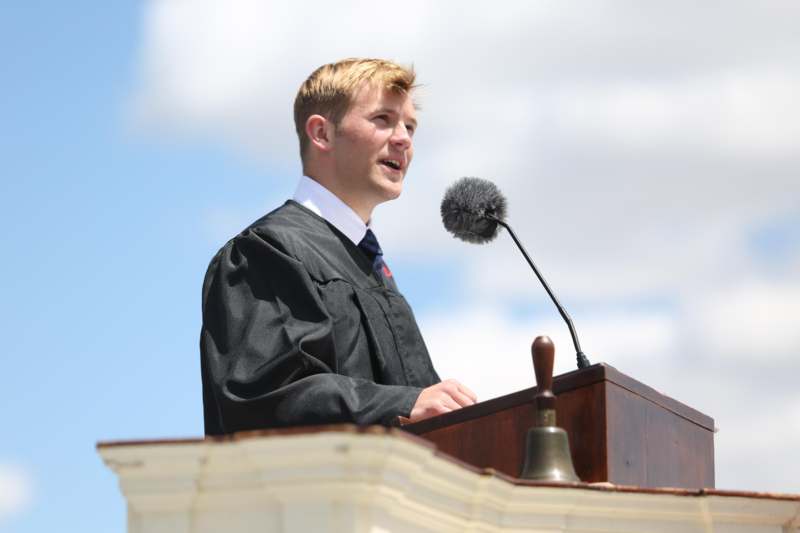 a man in a graduation gown speaking into a microphone