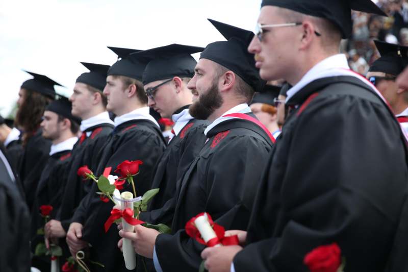 a group of graduates in black gowns and caps holding roses
