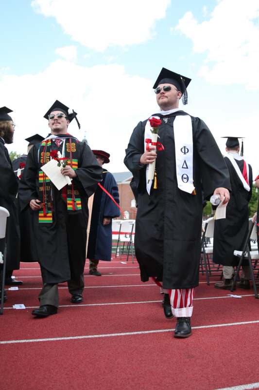 a group of men in graduation gowns and caps walking on a track