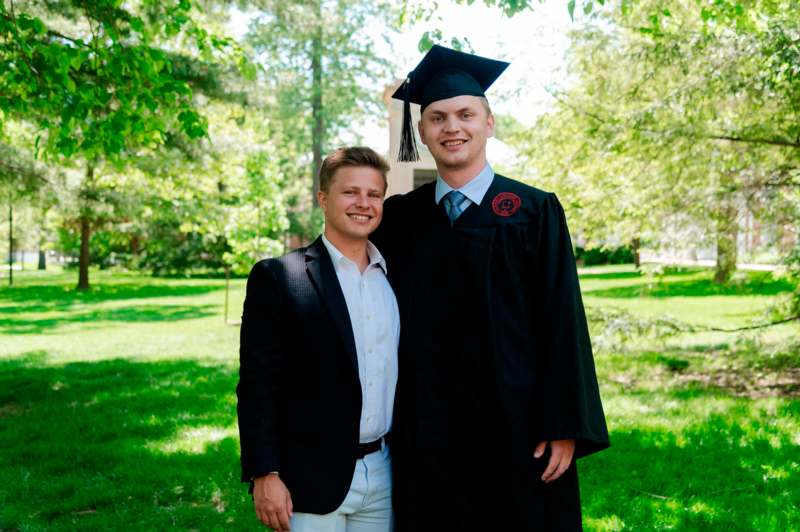 a man in a graduation gown and cap standing next to a man in a suit
