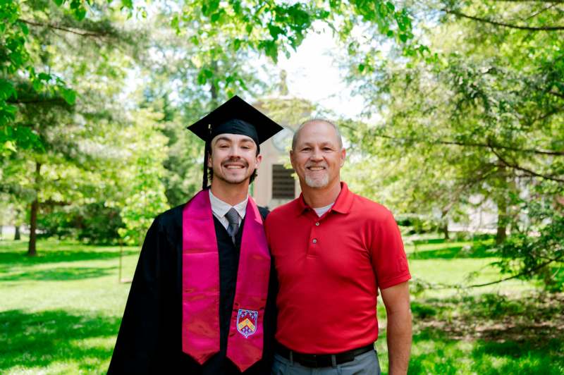 a man in a cap and gown standing next to a man in a red shirt