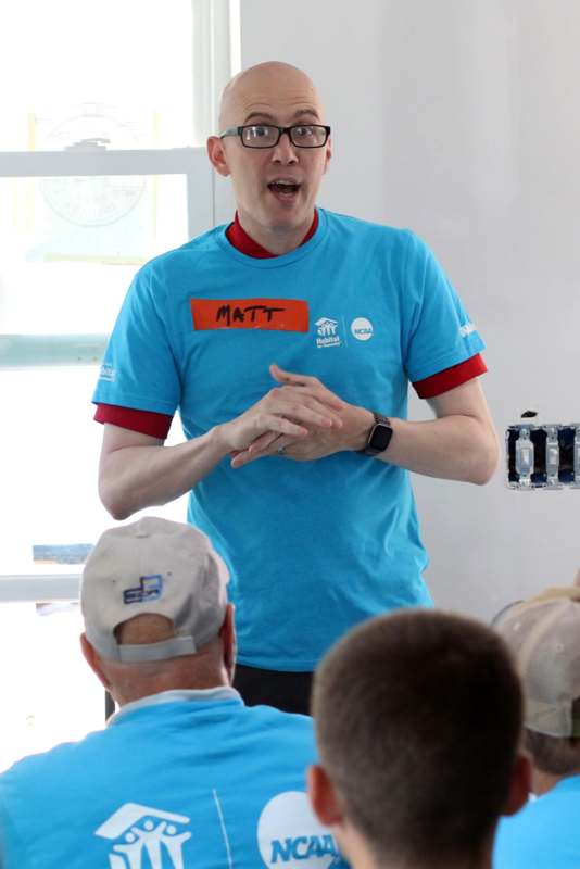 a man in a blue shirt speaking to a group of people