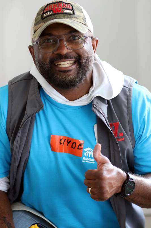 a man wearing glasses and a blue shirt giving a thumbs up