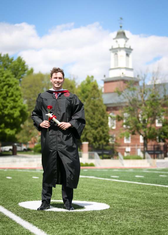 a man in a graduation gown holding a rose and a diploma