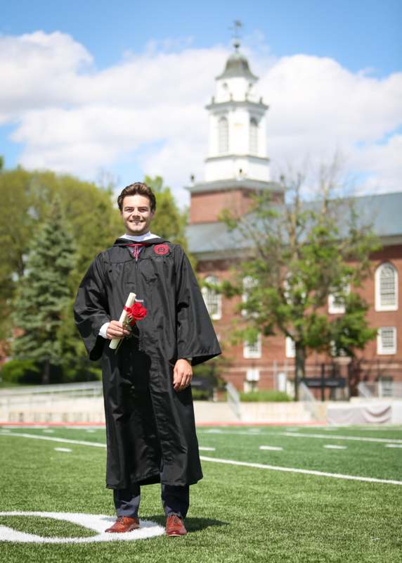 a man in a graduation gown holding a diploma and flowers