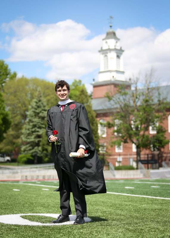 a man in a graduation gown holding a diploma and a flower