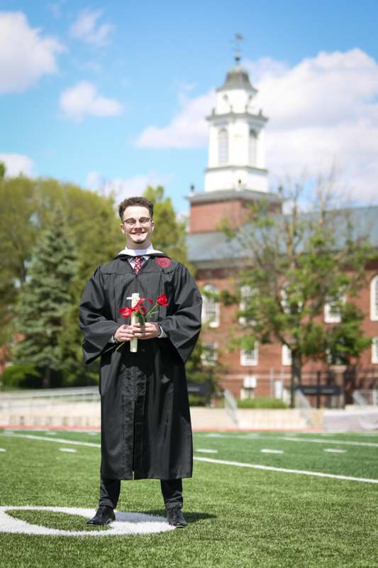 a man in a graduation gown holding a cross and flowers