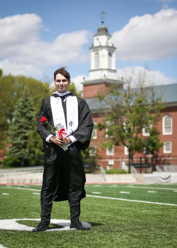 a man in a graduation gown holding a rose and a red rose