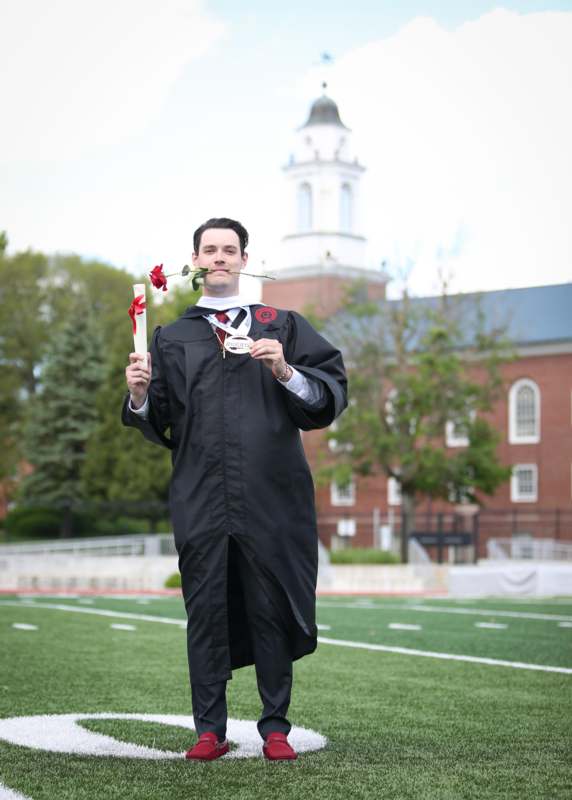 a man in a graduation gown holding a diploma and a rose