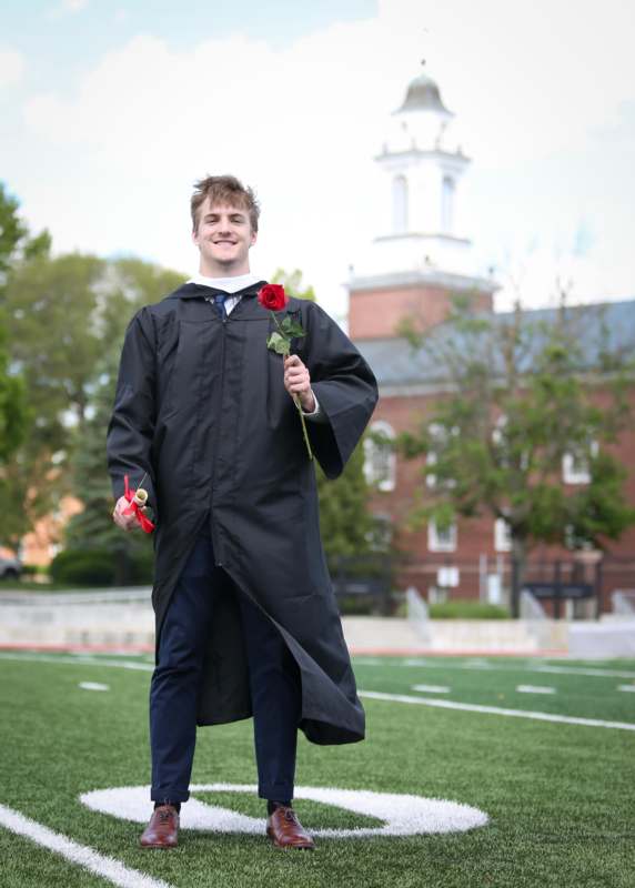a man in a graduation gown holding a rose