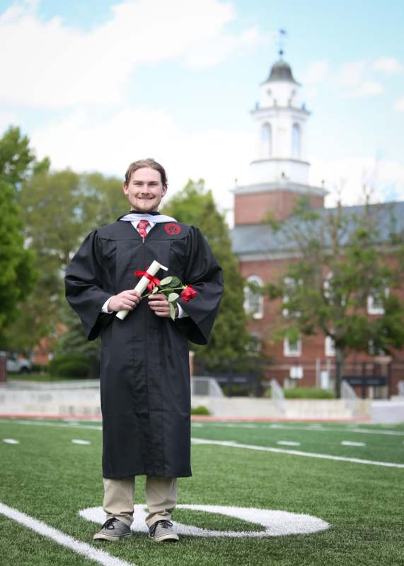 a man in a graduation gown holding a diploma and roses