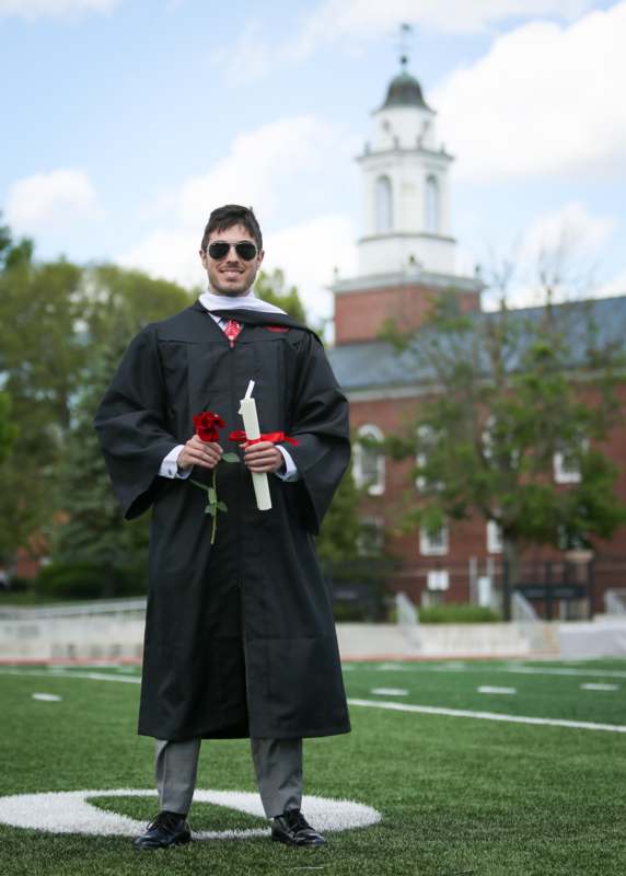 a man wearing a graduation gown and holding a rose