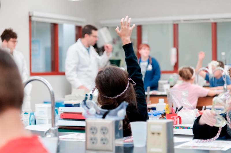 a woman raising her hand in a room with other people in the background