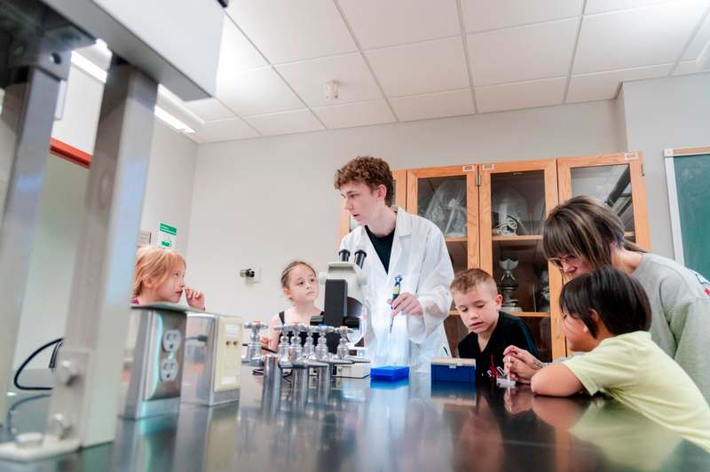 a man in a white coat and a group of kids in a lab
