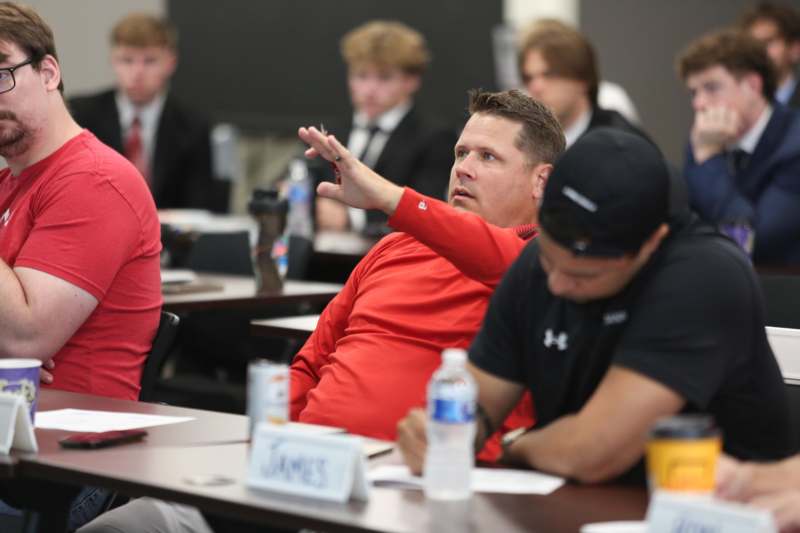 a man in a red shirt sitting at a table with other people in the background