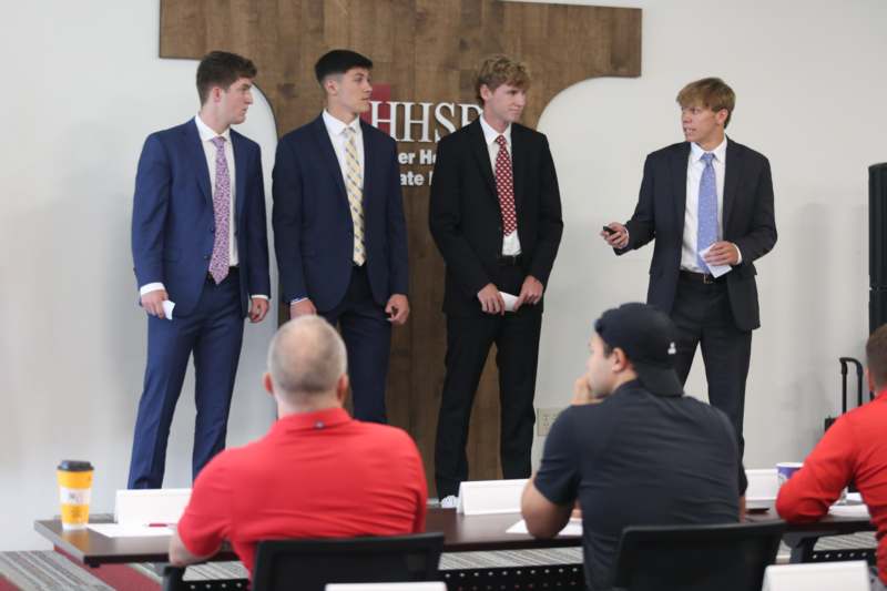 a group of men in suits standing in front of a man sitting at a table