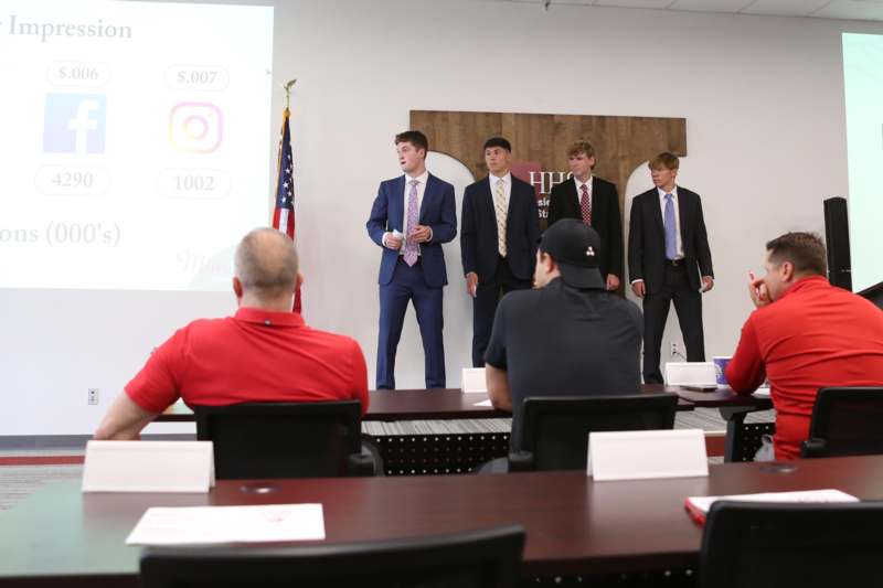 a group of men in suits standing in front of a room with a projector screen