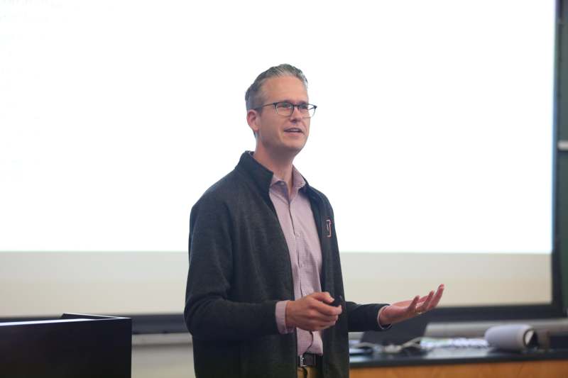 a man in a cardigan standing in front of a screen