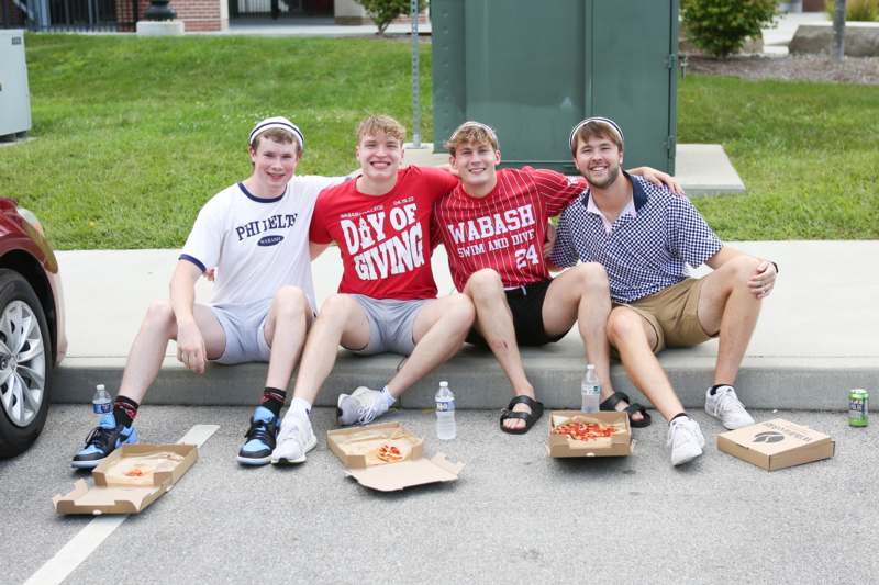 a group of men sitting on a curb with pizza boxes