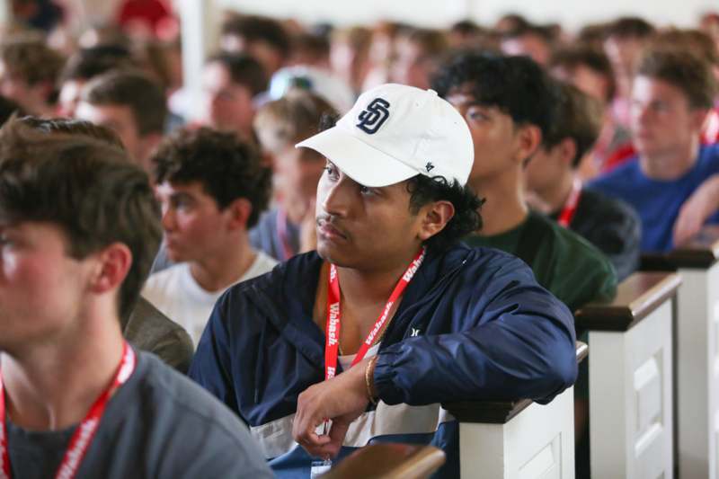 a man wearing a white hat and a blue jacket sitting in a room with other people