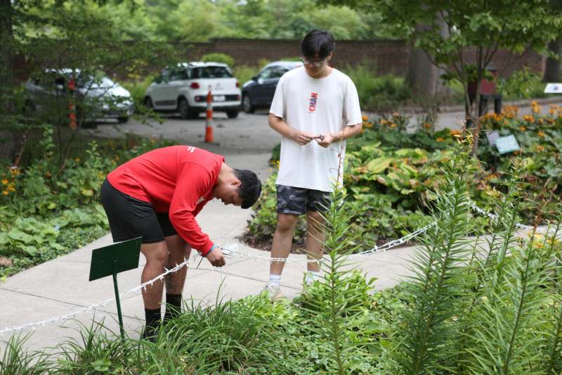 a man in shorts and a red shirt tying a rope around a man's neck