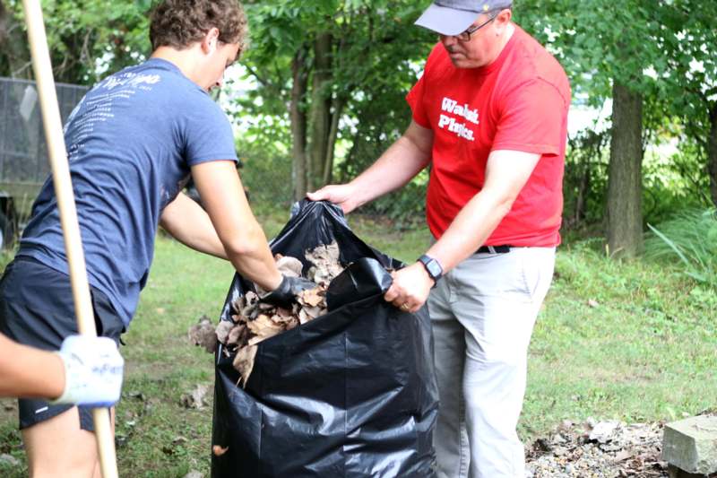 two men putting leaves in a bag