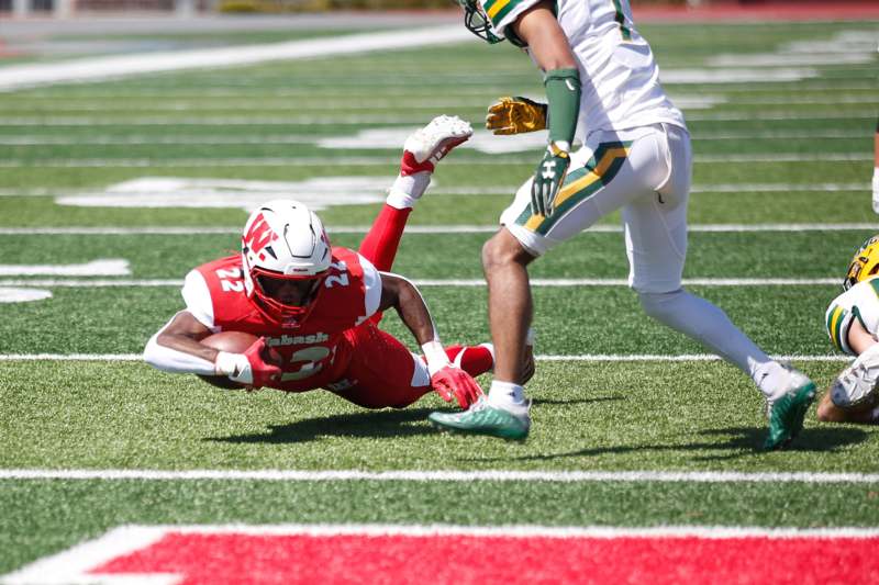 a football player falling to the ground while another player is running